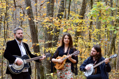 Das Bild zeigt die Mitglieder der Band South for Winter mit ihren Instrumenten in einem Wald stehend und sitzend vor einer Steinmauer.